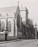 A black and white photograph of a street scene with the College buildings to the left
